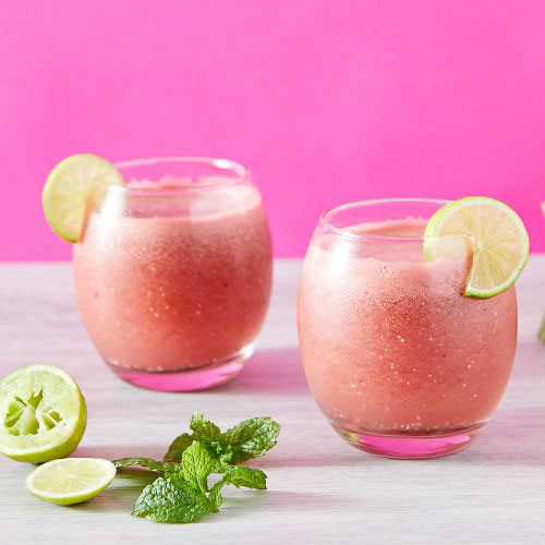 Frozen daquiri with a lime garnish on a white table with a pink background.